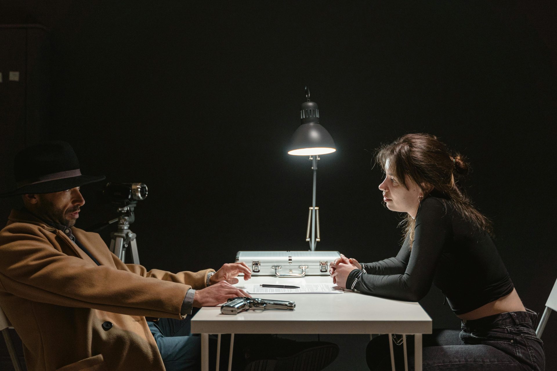 Tense interrogation scene with a man and woman in a dark room under harsh lighting.